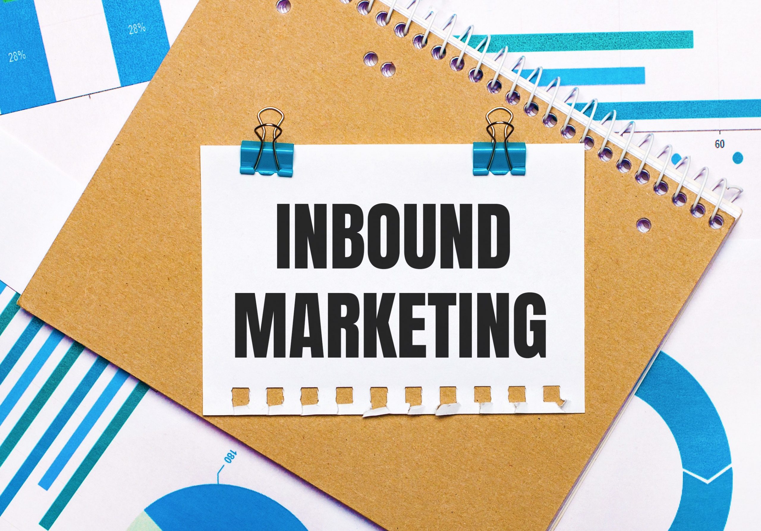 On the desktop are blue and light blue graphs and diagrams, a brown notebook and a sheet of paper with blue clips and INBOUND MARKETING text. View from above. Business concept